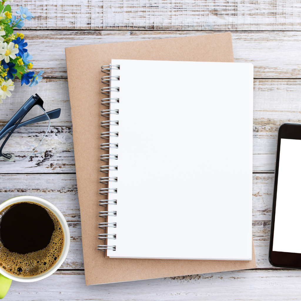 two journals stacked on each other with a cup of coffee and cell phone